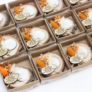 K&ouml;nnte beinhalten: Eine Sammlung von Babyparty-Gastgeschenken in kleinen Pappschachteln. Jede Schachtel enth&auml;lt eine Holzscheibe mit einer wei&szlig;en Kerze, Trockenblumen und einem Holzanh&auml;nger mit der Aufschrift "Thank You For Showering our Little Pumpkin David Baby Shower 12.04.2024."