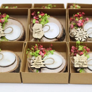May include: Six small gift boxes containing wooden candle holders decorated with dried flowers and a small wooden ornament. The ornaments have the text "Happy New Year 2023", "2023 Merry Christmas", and "Happy New Year 2023".
