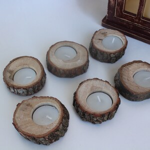 May include: Six rustic wooden candle holders with a natural bark finish. Each holder has a small, round indentation for a tea light candle.