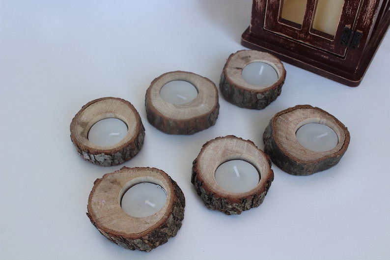 May include: Six rustic wooden candle holders with a natural bark finish. Each holder has a small, round indentation for a tea light candle.