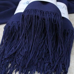 May include: A navy blue pashmina scarf with a long fringe. The scarf is folded in half and the fringe is visible on both sides.