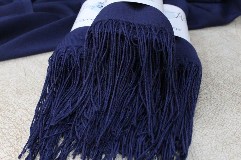 May include: A navy blue pashmina scarf with a long fringe. The scarf is folded in half and the fringe is visible on both sides.