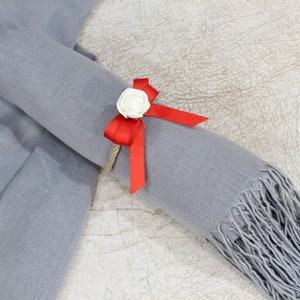 May include: A gray scarf with a red ribbon and a white flower tied around it.