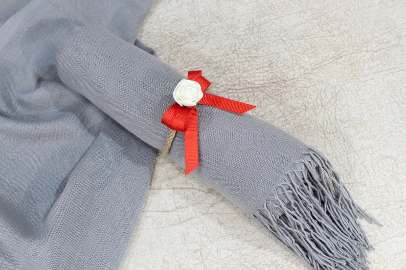 May include: A gray scarf with a red ribbon and a white flower tied around it.