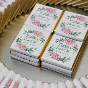 Puede incluir: Una bandeja de tabletas de chocolate envueltas individualmente con un dise&ntilde;o floral y el texto "Collette's Bridal Tea" y una fecha. Las tabletas de chocolate est&aacute;n envueltas en papel blanco con detalles de l&aacute;mina dorada.