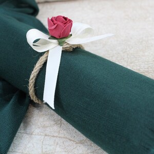 May include: A dark green fabric scarf with a white ribbon and a red fabric rose tied around it.