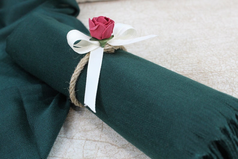 May include: A dark green fabric scarf with a white ribbon and a red fabric rose tied around it.