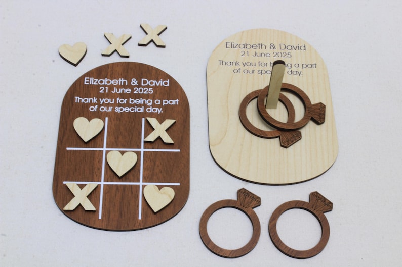 May include: Wooden wedding games set featuring a Tic-Tac-Toe board with hearts and X's, a ring toss game, and two ring-shaped game pieces. The set includes the text "Elizabeth & David 21 June 2025".