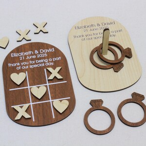 K&ouml;nnte beinhalten: Holz-Hochzeitsspiel-Set, einschlie&szlig;lich eines Tic-Tac-Toe-Bretts mit Herzen und X'en, einem Ringwurfspiel und zwei ringf&ouml;rmigen Dekorationen. Das Set tr&auml;gt die Namen "Elizabeth & David" und das Datum "21. Juni 2025".