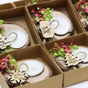 May include: An assortment of small, brown cardboard boxes with lids, each containing a wooden slice with a small white candle, a sprig of dried flowers, and a wooden ornament with a Christmas or New Year's message. The ornaments include a snowflake, a Christmas tree, and a New Year's tree.