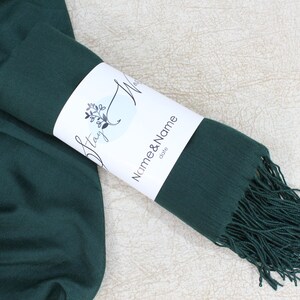 May include: A dark green scarf with fringe on the end. The scarf is rolled up and tied with a white label that says "Stay Wild" and "Name & Name" with the word "gifts" underneath.
