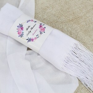 May include: White pashmina scarf with a fringe border. The scarf is rolled up and tied with a label that says "Hello Baby Shower" with a floral design.