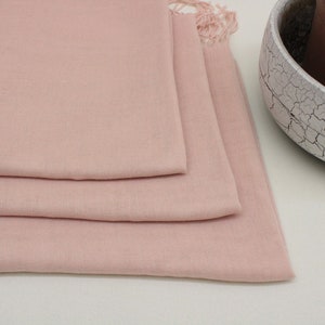 May include: A soft, pale pink scarf folded in three layers. The scarf has a fringed edge.