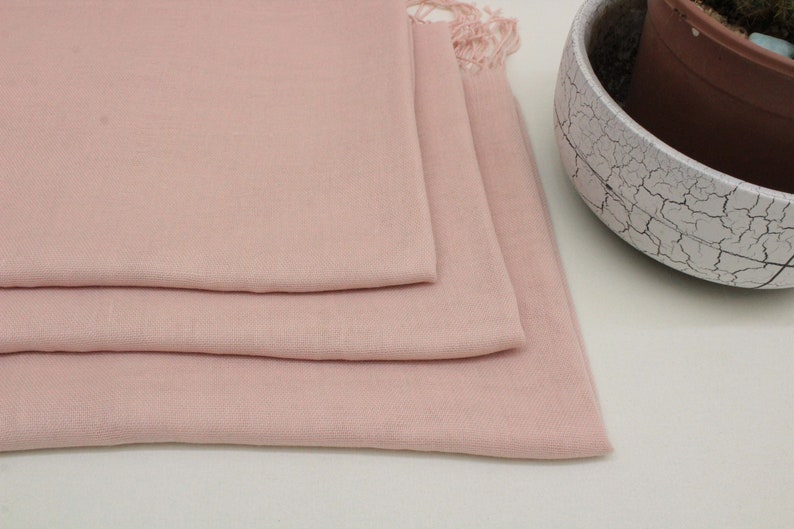 May include: A soft, pale pink scarf folded in three layers. The scarf has a fringed edge.