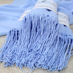 Pu&ograve; includere: Una sciarpa di pashmina blu chiaro con frange. La sciarpa &egrave; piegata e ha un'etichetta attaccata che dice "Name & Name".