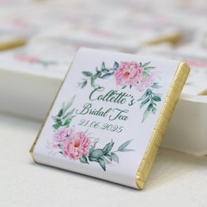 Puede incluir: Una barra de chocolate blanco con un borde dorado y un dise&ntilde;o floral. El texto en la barra de chocolate dice "Collette's Bridal Tea 21.06.2025".