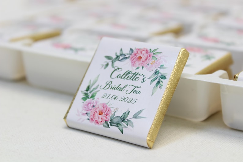 Puede incluir: Una barra de chocolate blanco con un borde dorado y un dise&ntilde;o floral. El texto en la barra de chocolate dice "Collette's Bridal Tea 21.06.2025".