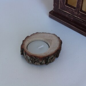 May include: A wooden candle holder made from a tree slice with a natural bark edge. The holder has a small, round indentation for a tea light candle.