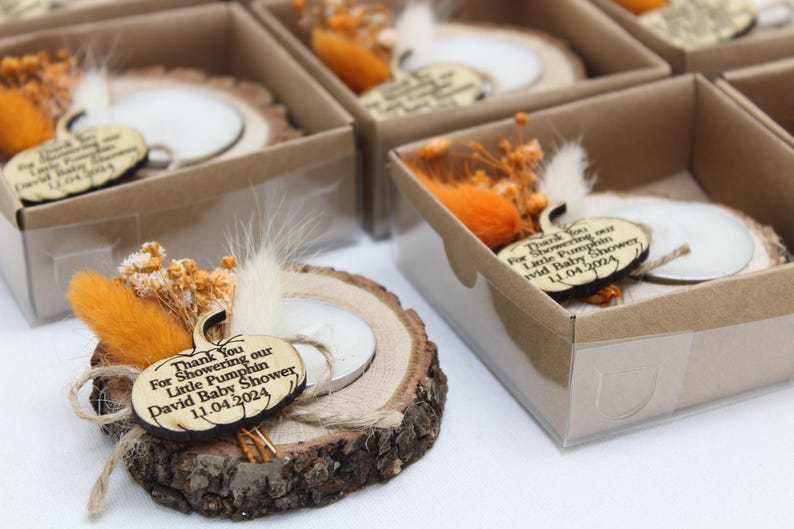 K&ouml;nnte beinhalten: Babyparty-Gastgeschenke aus Holz mit einem k&uuml;rbisf&ouml;rmigen Anh&auml;nger, einer kleinen Kerze und getrockneten Blumen. Jedes Gastgeschenk wird in einer kleinen Box mit transparentem Deckel pr&auml;sentiert. Der Anh&auml;nger tr&auml;gt die Aufschrift "Thank You For Showering our Little Pumpkin David Baby Shower 11.04.2024."