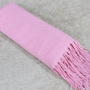 May include: A soft pink scarf with long fringe on the end. The scarf is rolled up and lying on a textured surface.