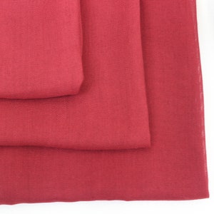 May include: Three pieces of red fabric folded on top of each other. The fabric has a smooth, slightly textured surface.