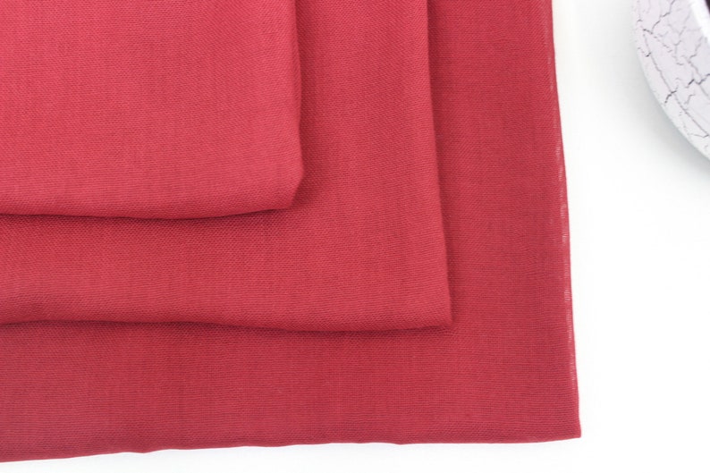 May include: Three pieces of red fabric folded on top of each other. The fabric has a smooth, slightly textured surface.