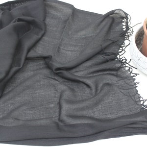 May include: A black sheer scarf with a fringed edge. The scarf is folded and laid out on a white surface.