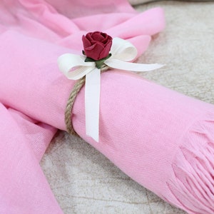 May include: A pink scarf with a white ribbon and a red rose tied around it.