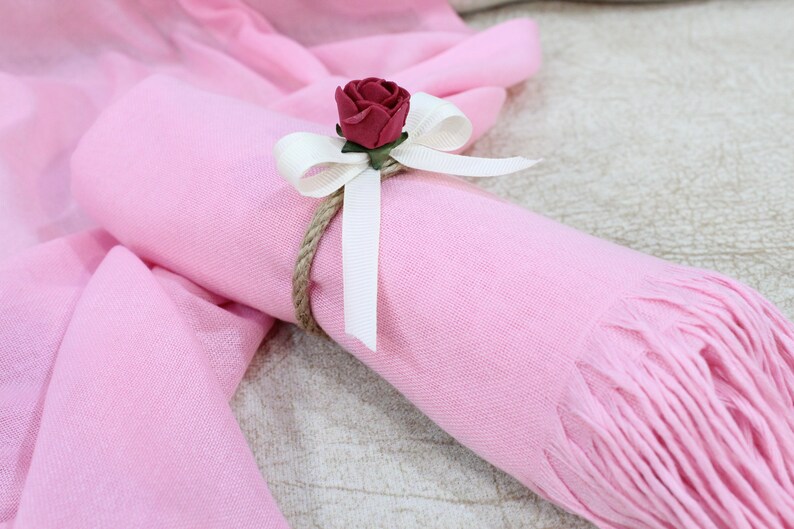 May include: A pink scarf with a white ribbon and a red rose tied around it.