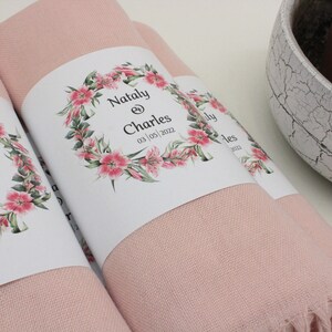 May include: Two pink pashmina scarves with white labels. The labels feature a floral wreath with the text "Nataly & Charles 03 | 05 | 2022".