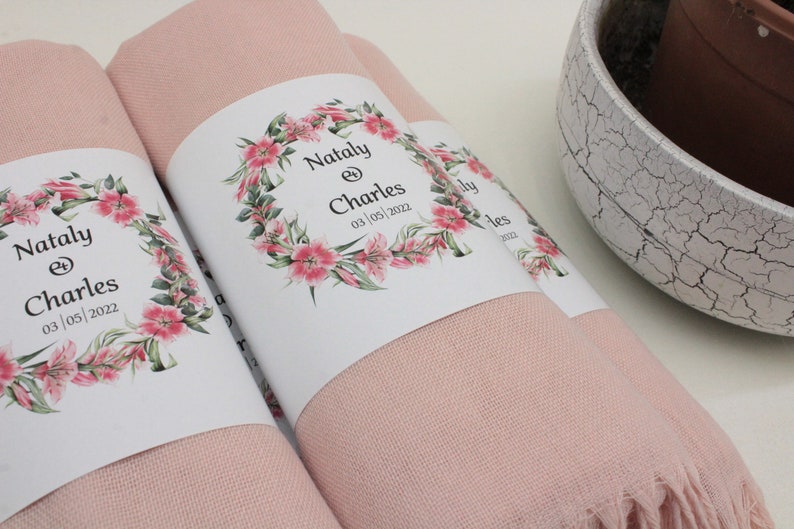 May include: Two pink pashmina scarves with white labels. The labels feature a floral wreath with the text "Nataly & Charles 03 | 05 | 2022".