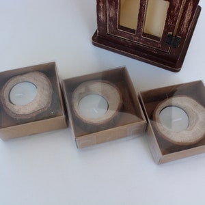 May include: Three small, round, wooden candle holders in clear plastic boxes. The candle holders are made from natural wood and have a rustic look.