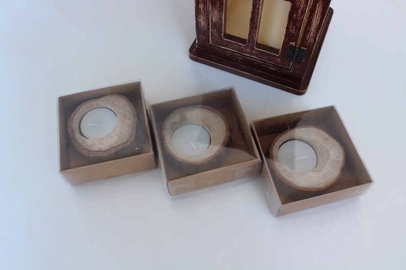 May include: Three small, round, wooden candle holders in clear plastic boxes. The candle holders are made from natural wood and have a rustic look.