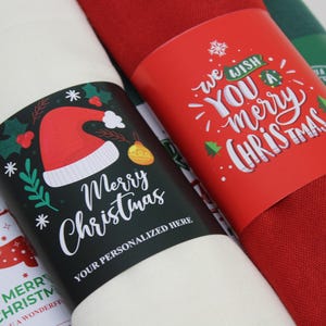 Pode incluir: Tr&ecirc;s argolas de guardanapo com tema natalino. Uma &eacute; vermelha com texto branco que diz "We wish you a merry Christmas". Outra &eacute; preta com texto branco que diz "Merry Christmas" e um chap&eacute;u de Papai Noel vermelho e branco. A &uacute;ltima &eacute; branca com texto vermelho e verde que diz "Merry Christmas" e uma rena vermelha.