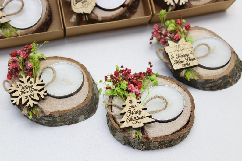 May include: Three wooden candle holders with small tea lights, decorated with sprigs of red and green flowers and a wooden snowflake or Christmas tree ornament. The ornaments have the text "Happy New Year 2024" or "2024 Merry Christmas".