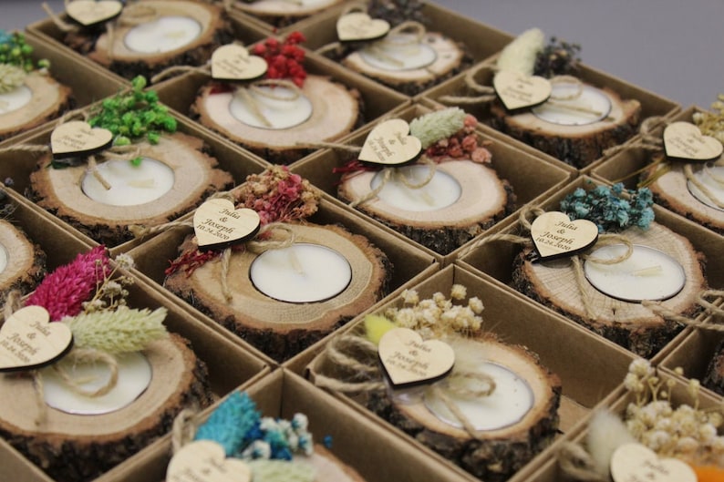 May include: Arrangement of tea light candles set in rustic wood slices, each adorned with dried flowers and a heart-shaped tag. The tags read "Julia & Joseph 10.24.2020". Presented in individual cardboard boxes, ideal for wedding favors or decorative accents.