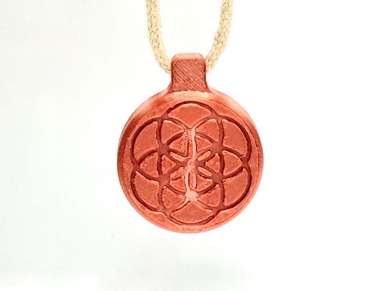 Op de afbeelding: Een roodbruine hangerketting met een cirkelvormig, gegraveerd ontwerp met een geometrisch bloemmotief. De hanger is bevestigd aan een beige koord. De ketting wordt gepresenteerd tegen een witte achtergrond.