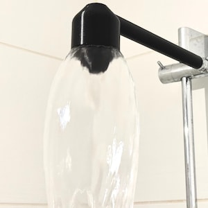 Könnte beinhalten: Ein transparenter Duschkopf aus Glas mit einem schwarzen Kunststoffdeckel, befestigt an einem silbernen Duscharm und einem Schlauch.