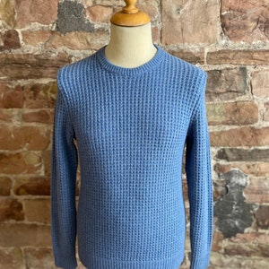 May include: A light blue waffle knit jumper with long sleeves and a crew neck.