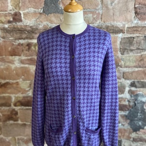 May include: A purple and blue cardigan with a houndstooth pattern. The cardigan has a button-up front and two pockets.