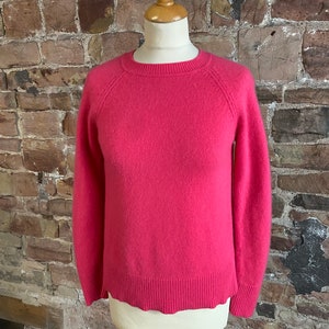 May include: A pink cashmere jumper with a round neckline and long sleeves. The jumper has a ribbed hem and cuffs.