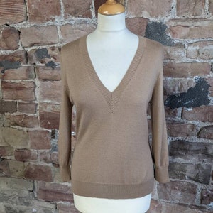 May include: A light brown v-neck sweater with long sleeves.