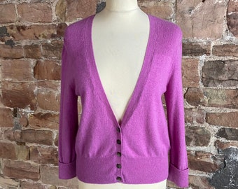 May include: A purple cardigan with a v-neck and button closure. The cardigan has long sleeves and a ribbed texture.