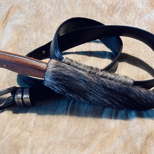 May include: A brown handled knife with a black leather sheath and a black belt. The sheath is made of fur.