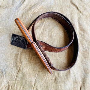 May include: A brown leather belt with a silver buckle that says "PHILMONT" and a wooden knife with a silver blade.