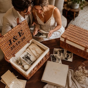 Newlywed couple looking through photographs beside a personalised wicker wedding memory box and photo album for storing wedding cards, photos and special keepsakes.