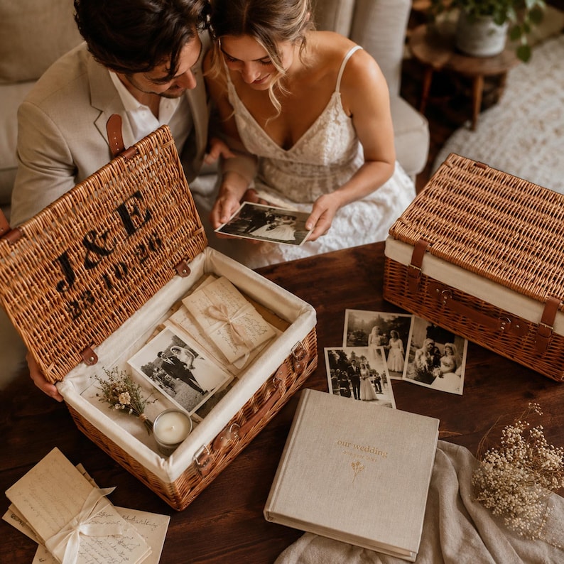 Newlywed couple looking through photographs beside a personalised wicker wedding memory box and photo album for storing wedding cards, photos and special keepsakes.