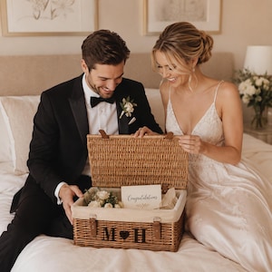 Bride and groom opening a personalised wicker wedding memory box, a thoughtful newlywed gift hamper for storing cards, photographs and keepsakes after the wedding.