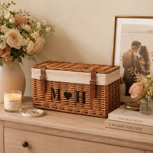 Closed personalised wicker wedding keepsake box with couple initials, cream cotton trim and brown vegan leather straps, styled as elegant post-wedding home storage.