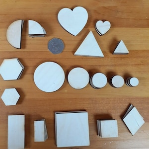 May include: A set of wooden shapes in various sizes and designs, including circles, hearts, squares, triangles, and hexagons. The shapes are all white and have a black outline.